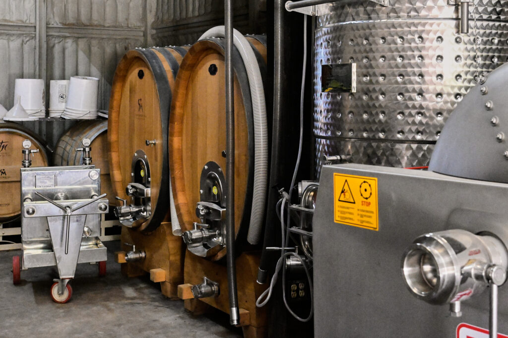 Toneles grandes de vino en el interior de Cava Maciel, usados para el añejamiento en madera en un espacio amplio y con luz tenue.